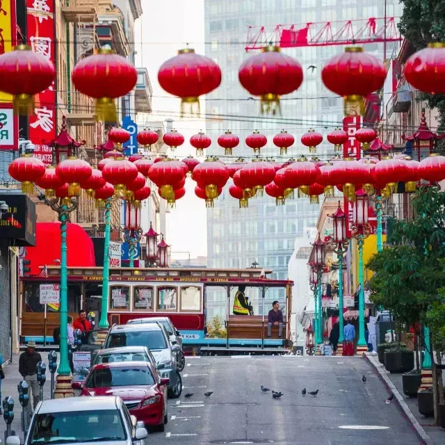 Uma rua montanhosa na 唐人街 de 贝博体彩app é retratada com lanternas vermelhas penduradas e um bonde passando.